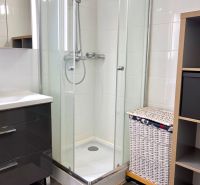 Badezimmer mit Dusche, Schrank und Wäschekorb in einer Zweizimmerwohnung.
