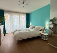 Helles Schlafzimmer mit türkisfarbener Wand, Holzboden und Spiegelschrank in einer Vierzimmerwohnung.