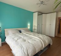 Helles Schlafzimmer mit türkisfarbener Wand, weißen Schränken und Holzboden.