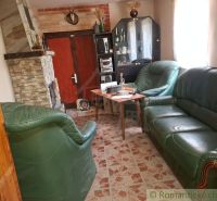 Innenraum einer Hütte mit Kamin, Ledersofa und einer Vitrine auf einem Boden mit Holzdekor.
