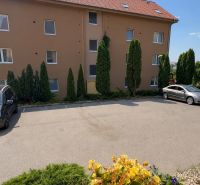 Parkplatz vor einem Wohnhaus in Veľký Lapáš mit Autos und umliegendem Grün.