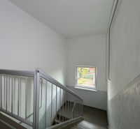 Eine Treppe mit Fenster in einer 2-Zimmer-Wohnung, die Wände sind weiß mit einem Metallgeländer.