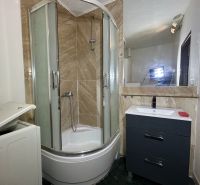 Badezimmer mit Dusche, dunklem Schrank und Spiegel in einer Zweizimmerwohnung.