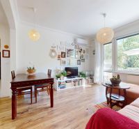 Wohnzimmer in einer 3-Zimmer-Wohnung mit Holzboden, großem Fenster und dekorativen Elementen.