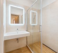 Badezimmer in einer 3-Zimmer-Wohnung mit Waschbecken und Duschkabine, Boden mit Holzdekor.