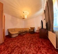 Wohnzimmer in einem Einfamilienhaus mit Ecksofa und bordeauxfarbenem Teppich.