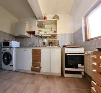 Küche in einem Einfamilienhaus mit Keramikboden, Schränken, Herd, Mikrowelle und Waschmaschine.
