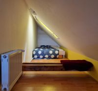 Dachzimmer mit schräger Decke, Heizkörper und Boden mit Holzdekor.