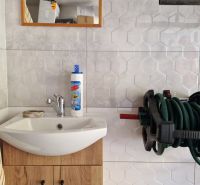 Badezimmer in einer 2-Zimmer-Wohnung mit Waschbecken, Spiegel und Wandhalterung für einen Schlauch.