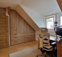 Dachboden mit Holzelementen, Schreibtisch und Stuhl in einer 2-Zimmer-Wohnung.