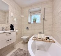 Badezimmer mit Badewanne und Waschbecken in einer 2-Zimmer-Wohnung, beige Fliesen.