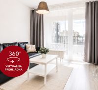Wohnzimmer in einer Zweizimmerwohnung mit schwarzem Sofa, Fernseher und Balkon.