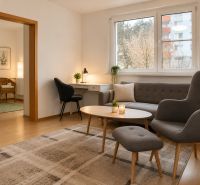 Wohnzimmer in einer 2-Zimmer-Wohnung mit bequemen Sitzgelegenheiten und einem Tisch.