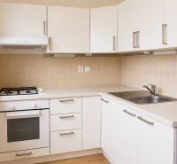 Küche mit weißen Schränken und Geräten in einer Zweizimmerwohnung, Boden mit Holzdekor.