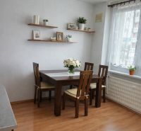 Essbereich mit Tisch, Stühlen und Regalen auf einem Boden mit Holzdekor in einer 3-Zimmer-Wohnung.