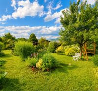 Ein Garten bei einer Hütte in Žilina mit Bäumen, Blumen und weißen Gartenmöbeln.