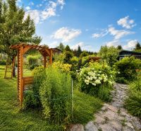 Ein Garten bei einer Hütte in Žilina mit einer Holzpergola und Blumenbeeten.