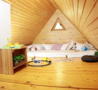 Der Dachboden der Hütte mit einem Boden in Holzoptik enthält Matratzen, Spielzeug und einen Tisch.