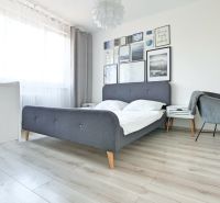 Helles Schlafzimmer mit Bett, Sessel und Boden in Holzoptik, in einer 2-Zimmer-Wohnung.