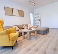 Wohnzimmer mit Holzboden, gelbem Sessel und Sofa in einer Zweizimmerwohnung.