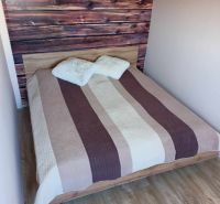 Ehebett mit gestreifter Überdecke und Boden in Holzoptik.
