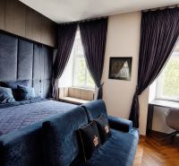 Luxuriöses Schlafzimmer mit dunklen Vorhängen und Schreibtisch in einer 2-Zimmer-Wohnung.