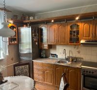 Küche in einer 3-Zimmer-Wohnung mit Holzmöbeln, dekorativem Vorhang und Esstisch.