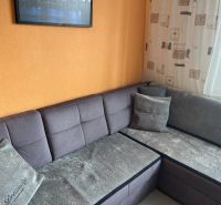 Ein graues Sofa in der Ecke des Wohnzimmers in einer Dreizimmerwohnung mit einer orangefarbenen Wand.