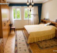 Schlafzimmer mit Holzboden, gelber Tagesdecke und großen Fenstern in einem Einfamilienhaus.