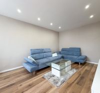 Wohnzimmer mit blauer Couch und Glastisch, Boden mit Holzdekor.