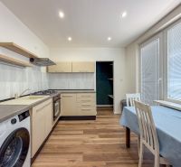 Küche in einer 2-Zimmer-Wohnung mit Geräten, Esstisch und Bodenbelag in Holzoptik.