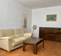 Wohnzimmer mit cremefarbenem Sofa, Holztisch und Schrank auf einem Boden mit Holzdekor.
