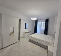 Helles Schlafzimmer mit Bett, Schrank, Fliesen und Vorhängen in einer 2-Zimmer-Wohnung.