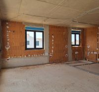 Innenraum einer im Bau befindlichen 3-Zimmer-Wohnung mit nackten Ziegelwänden und Kunststofffenstern.