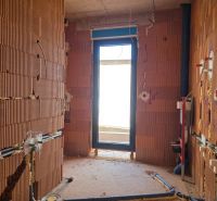 Ein unvollendeter Raum mit rohen Ziegelwänden und einem Ausgang zum Balkon in einer 3-Zimmer-Wohnung.