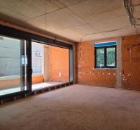 Unvollendete 3-Zimmer-Wohnung mit großen Fenstern und freiliegenden Ziegeln ohne Boden.