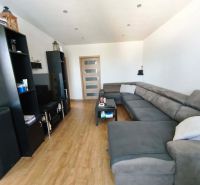 Wohnzimmer mit großer Couch, Holzboden und schwarzen Möbeln in einer 3-Zimmer-Wohnung.