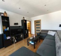Wohnzimmer in einer 3-Zimmer-Wohnung mit großem Sofa, Fernseher und Holzboden.