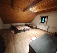 Ein Zimmer mit drei Betten, einem Boden in Holzoptik und einer schrägen Holzdecke in einer Hütte.