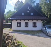 Ein Ferienhaus in Špania Dolina mit weißer Fassade und Satellitenschüssel, umgeben von Grün.