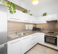 Küche in einer 2-Zimmer-Wohnung mit weißen Schränken und Holzelementen.