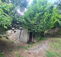 Ein Einfamilienhaus in Svodín mit einer Felswand, einer Steinmauer und grünen Bäumen im Garten.