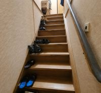 Eine Treppe mit einem Boden in Holzoptik voller Schuhe in einem Einfamilienhaus.