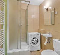 Badezimmer in einer Einzimmerwohnung mit Duschkabine und Waschmaschine, beige Fliesen.