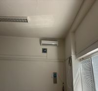 Deckenklimaanlage in Geschäftsräumen mit weißen Jalousien an den Fenstern.