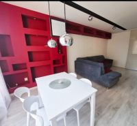 Innenraum einer 3-Zimmer-Wohnung mit roten Regalen, einem weißen Tisch und einem grauen Sofa.