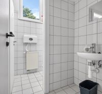 Toilette mit weißen Fliesen und Waschbecken in Geschäftsräumen.