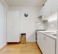 Küche in einer 3-Zimmer-Wohnung mit weißen Schränken, Holzboden und einer Uhr an der Wand.