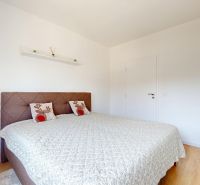 Schlafzimmer mit Bett, Sessel und dekorativen Kissen in einer 3-Zimmer-Wohnung, Boden mit Holzdekor.
