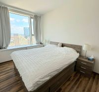 Ein Zimmer mit einem großen Fenster, einem Bett und einem Boden mit Holzdekor in einer 3-Zimmer-Wohnung.